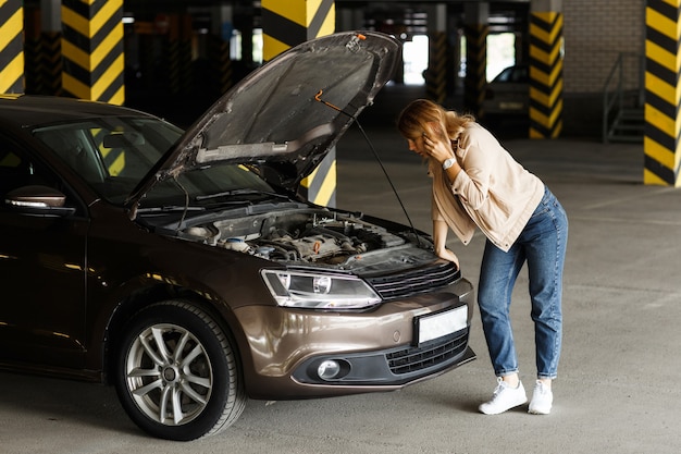 Foto autista preoccupata in jeans e giacca a vento, che chiede aiuto nel parcheggio per aiutare con il guasto dell'auto