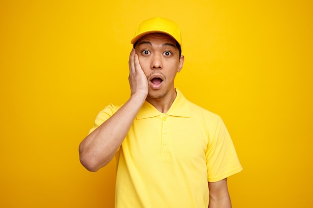 Concerned young delivery man wearing cap and uniform keeping hand on face 