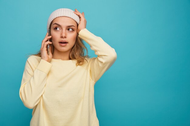 Photo concerned young girl wearing winter hat talking on phone keeping hand on head looking at side