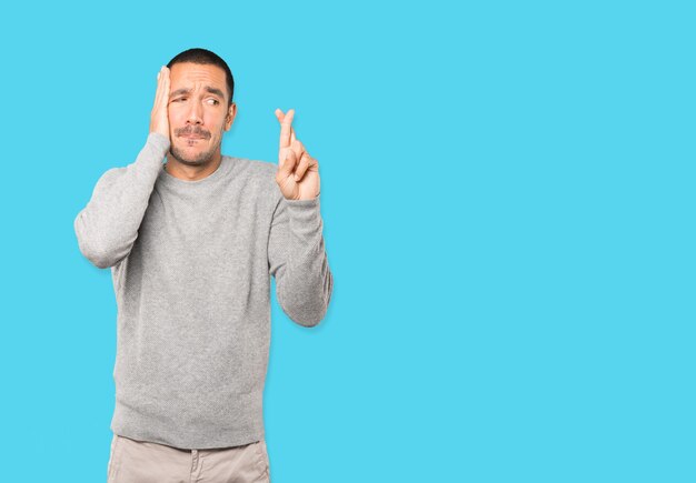 Concerned young man doing a crossed fingers gesture