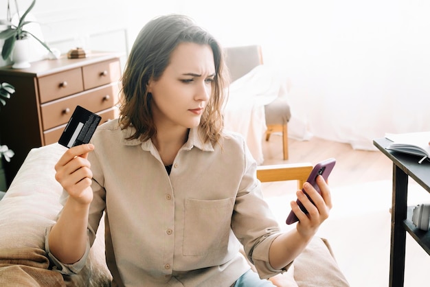 Обеспокоенная молодая женщина с кредитной картой, печатающая на смартфоне, сталкивается с проблемами с онлайн-заказами