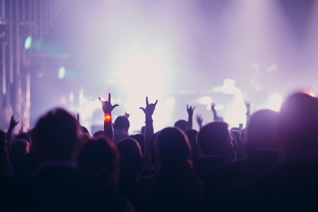 Concert, event or party concept. People with hands up at the scene, spotlight, colored lilac light.