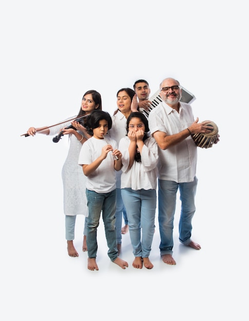 Concert of Indian family of six playing music instruments in a group and senior lady singing, standing against white background