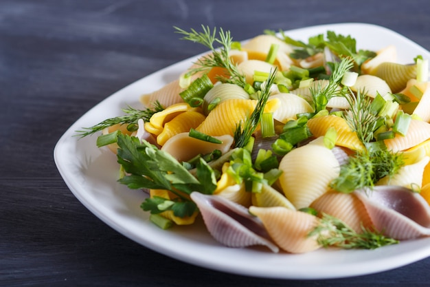 Conchiglie colored pasta with fresh greengrocery on black wooden table.