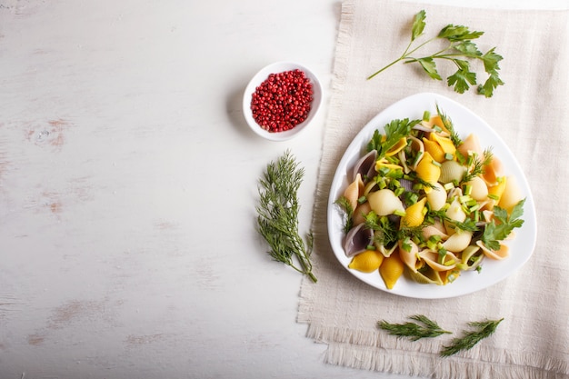 白い木のリネンのテーブルクロスの上の新鮮なgreengroceryとConchiglie色のパスタ