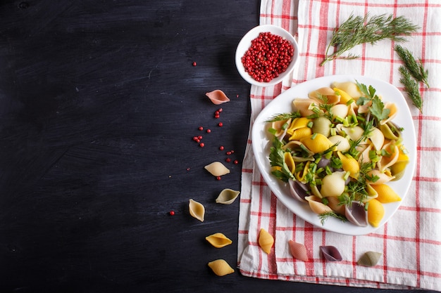 Conchiglie gekleurde pasta met verse groente op een linnen tafelkleed op zwart hout