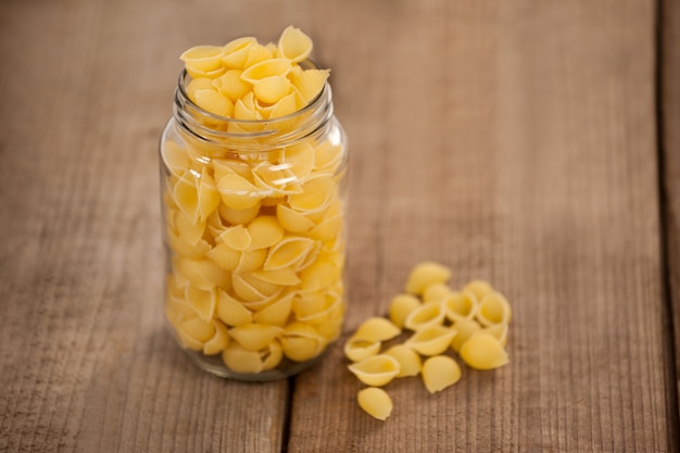 Conchiglie pasta spilled out of glass jar on wooden surface