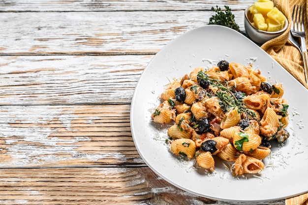 Итальянская паста Conchiglie rigate с помидорами, оливками, каперсами и анчоусами. Белый фон. Вид сверху. Скопируйте пространство.