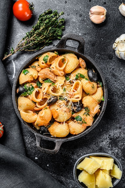 Conchiglie rigate pasta puttanesca met ansjovis, tomaten, knoflook en zwarte olijven. Zwarte achtergrond. Bovenaanzicht.