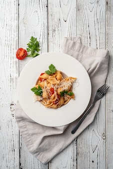 Conchiglioni con pomodorini formaggio e prezzemolo in piatto bianco su fondo di legno Foto Premium