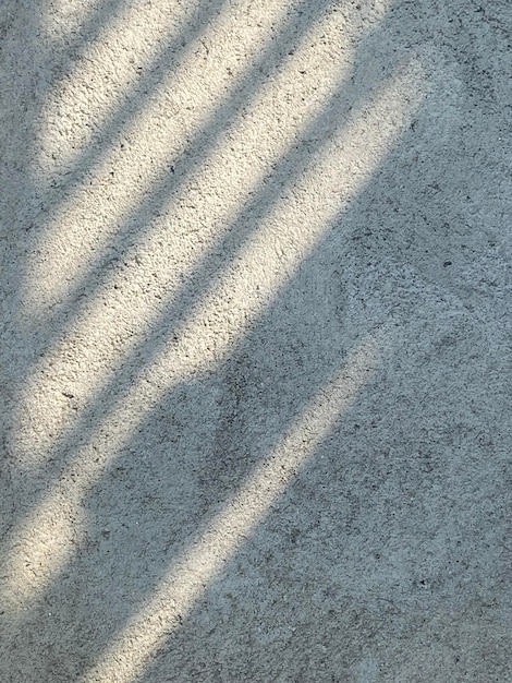 A concrete floor with a shadow of a fence and a man walking on it.