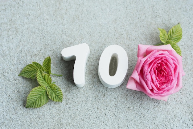 Фото Бетонный номер 70 и красивая роза с лепестками и сердечками на бетонном сером фоне.