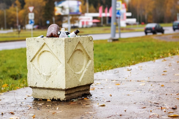 Concrete trash bin with empty bottles on road background