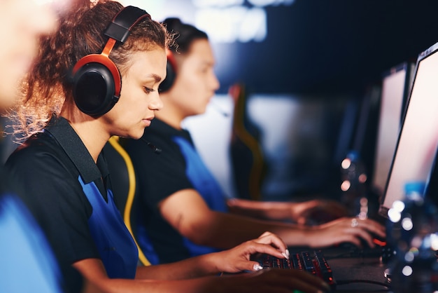 Concurrentie. Zijaanzicht van een gefocust gemengd rasmeisje, vrouwelijke cybersport-gamer die een koptelefoon draagt die online videogames speelt, die met een team deelneemt aan een eSport-toernooi