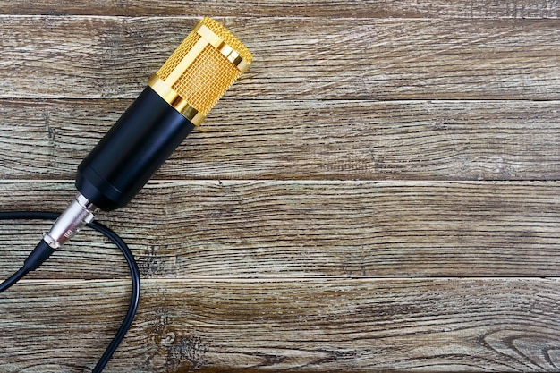Foto condensator gouden microfoon met kabel op een houten tafel met kopie ruimte. muzikaal thema. plat leggen. bovenaanzicht.