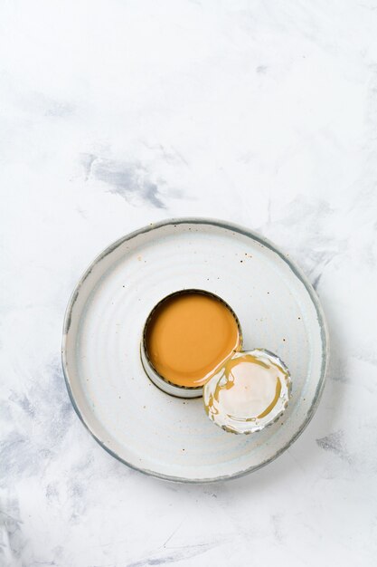 Condensed or evaporated milk in open tin on light concrete table. Top view.