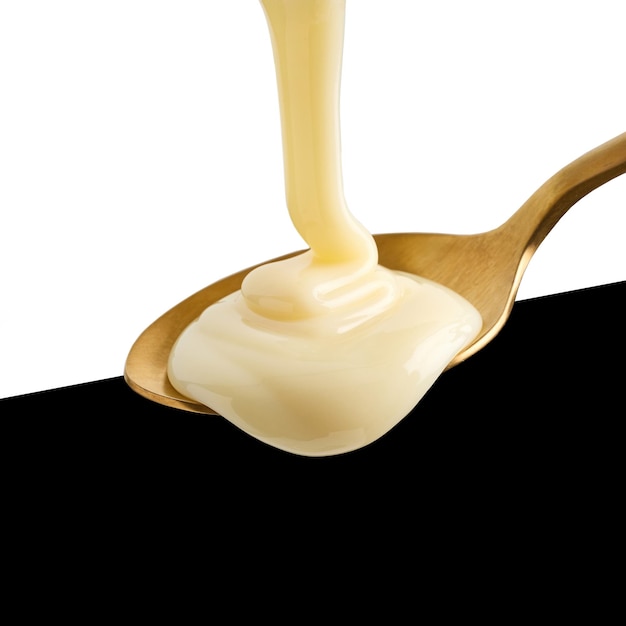 Photo condensed milk pouring into golden spoon isolated on black and white background