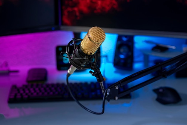 Condenser microphone in gamer setup with monitors keyboard mouse and colored lights