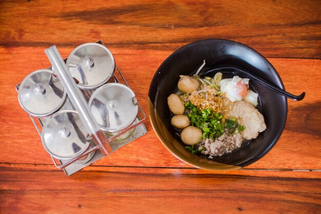 Condiment bottles near delicious spicy noodles put on a black cup on a wooden table