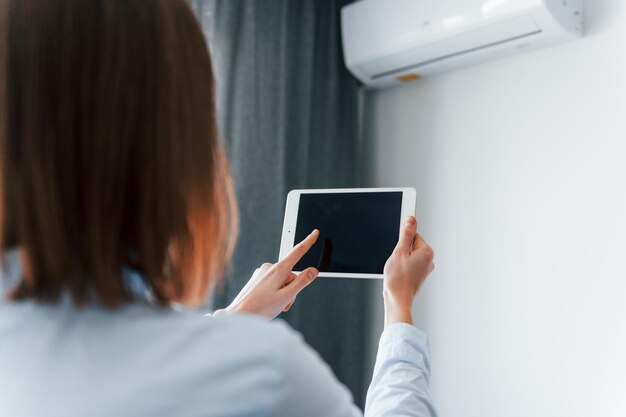 Conditioner bedienen via tablet Jonge vrouw is overdag binnenshuis in de kamer van een modern huis