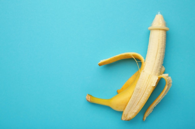 Condom and banana on blue background with copy space