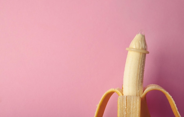 Foto preservativo e banana su sfondo rosa con spazio di copia