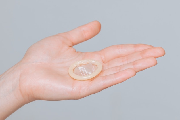 The condom lies on the female hand on gray background