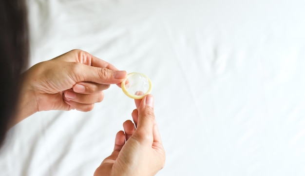 Preservativo in mano di donna con un letto bianco sfondo sfocato concetto di malattie sessualmente trasmissibili
