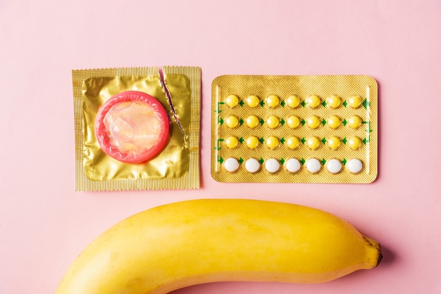 condom on wrapper pack, banana and contraceptive pill, flat lay