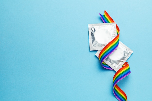Condoms and LGBT rainbow ribbon pride tape symbol. Blue background. Copy space for text.