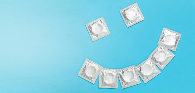 Condoms in packaging in the form of smile on blue background. Copy space for text.