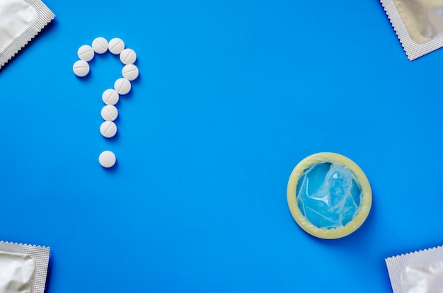 Condoom en vraagteken van tabletten op een blauwe achtergrond