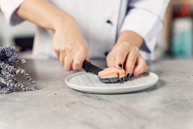 The confectioner cuts macaron with a knife. Close up female chef's hands. Preparing of tasty dessert.