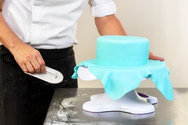 Confectioner decorating a wedding cake with blue fondant.