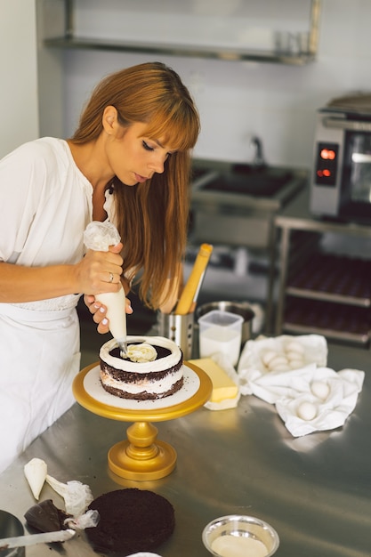 写真 菓子屋の女の子が白いクリームとチョコレートのクッキングケーキでケーキビスケットを準備しています