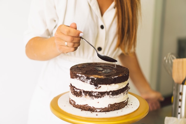 菓子屋の女の子が白いクリームとチョコレートのクッキングケーキでケーキビスケットを準備しています