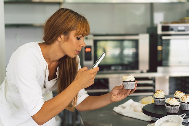 Photo confectioner girl photographing cupcake for her blog girl makes a photo of cupcakes on a smartphone