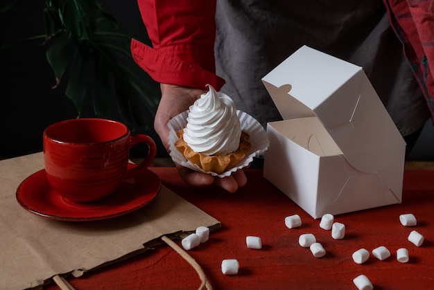 Confectioner holding white paper box with white cake near red table