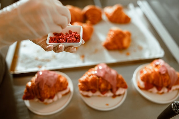 Confectioner holds bowl with sprinklings above delicious croissants on counter