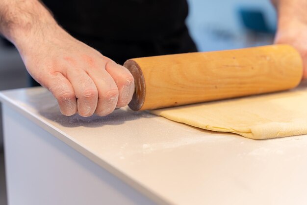 Uomo del pasticcere che cucina croissant fatti in casa che impastano la pasta sfoglia con il lavoro dello strumento a casa