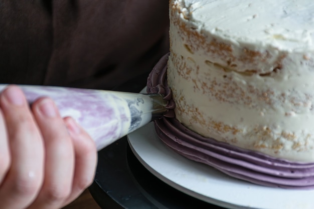 Il pasticcere usa la bocchetta della glassa per decorare la torta alla crema al burro viola.