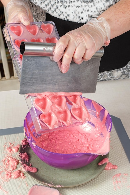 Photo confectioner using a spatula to remove excess strawberry ganache in a polycarbonate pan.