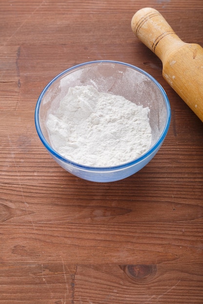 Confectionery flour in a bowl on a wooden table next to a rolling pin