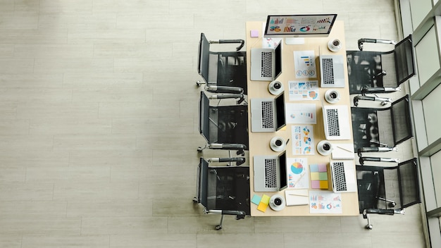 Conference meeting room working table in company office full of laptop notebook computers black hot coffee cups and report data paperwork documents and black chairs with copy space on wooden floor.