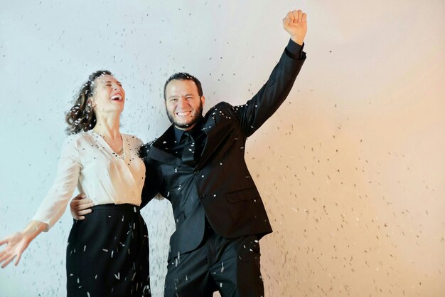 Photo confetti falling over cheerful friends standing against wall during christmas