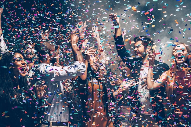 Photo confetti fun. group of beautiful young people throwing colorful confetti while dancing and looking happy