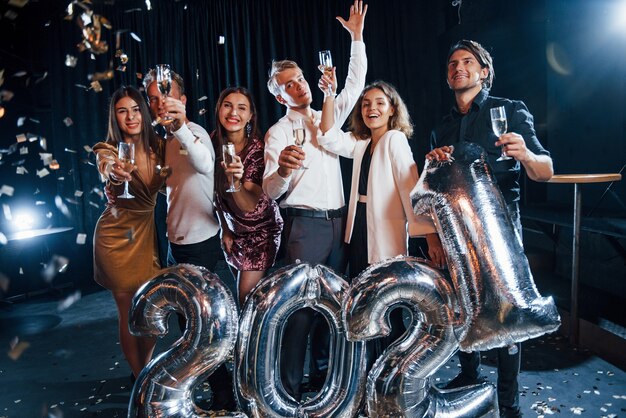 Confetti hangt in de lucht. Vrolijke groep mensen met drankjes en ballonnen in handen die het nieuwe 2021-jaar vieren.
