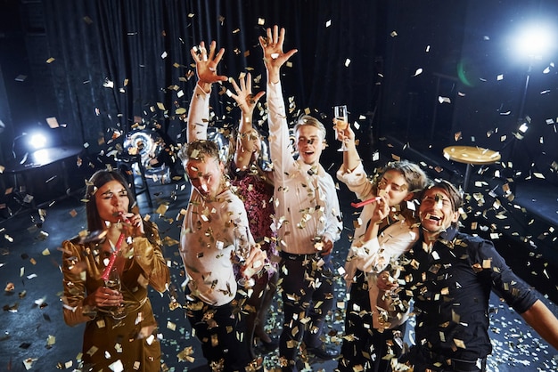 Confetti is in the air. Group of cheerful friends celebrating new year indoors with drinks in hands.