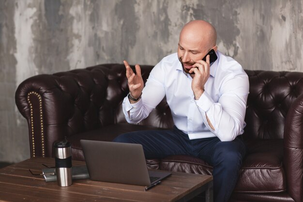 Confident adult man talks on the phone sitting at the computer