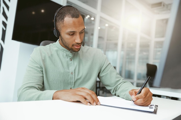 Confident African businessman taking notes while sitting in modern office